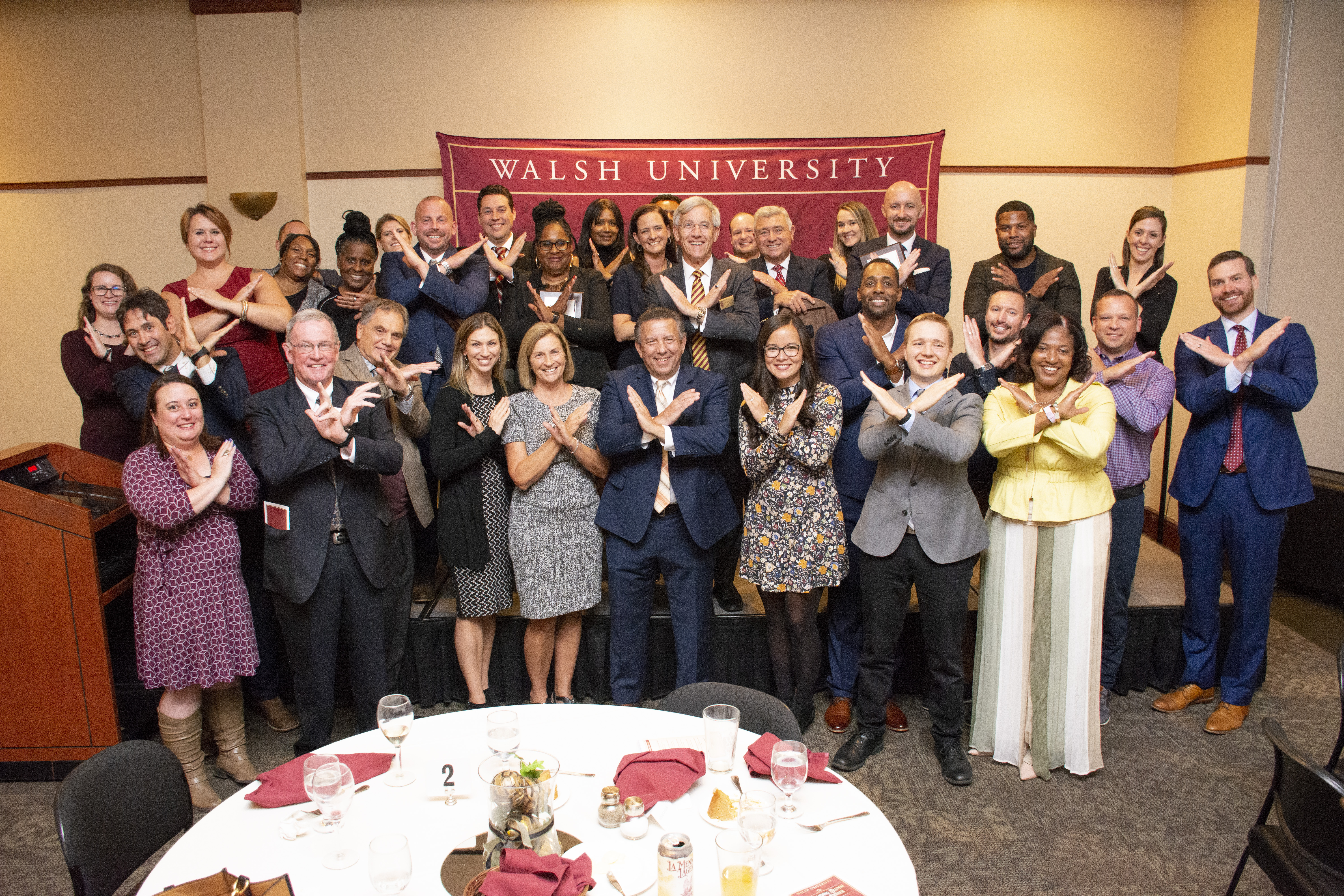 group of Alumni displaying swords up hand gesture (forearms crossed in front of them)